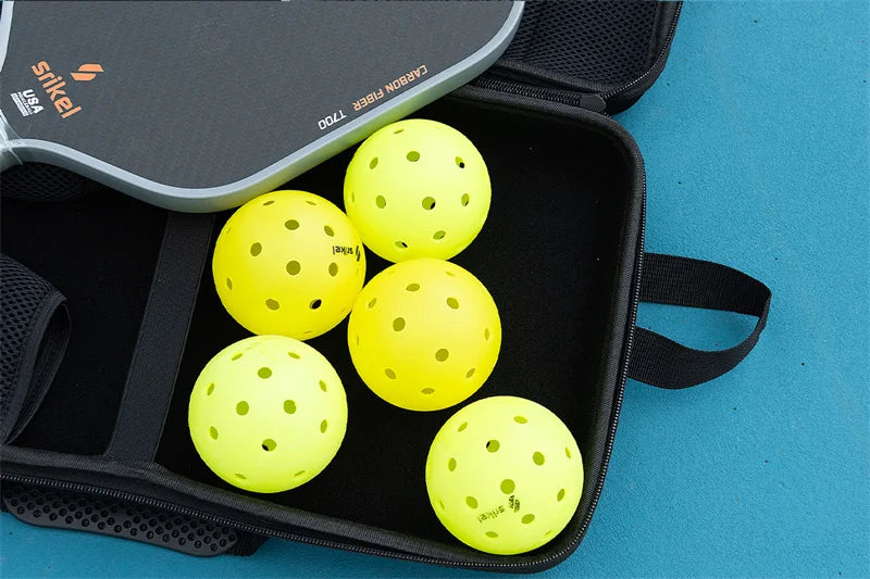 Five yellow perforated pickleballs and part of a pickleball paddle in a black carrying case.