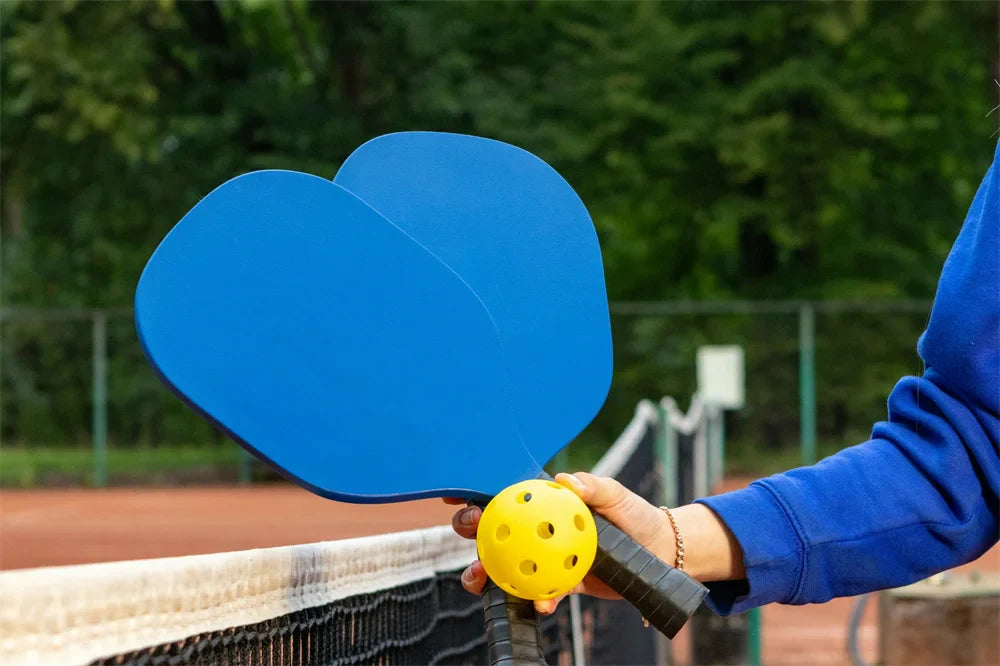 there is one person grab two blue pickleballs and one yellow pickleball stand in front of the net