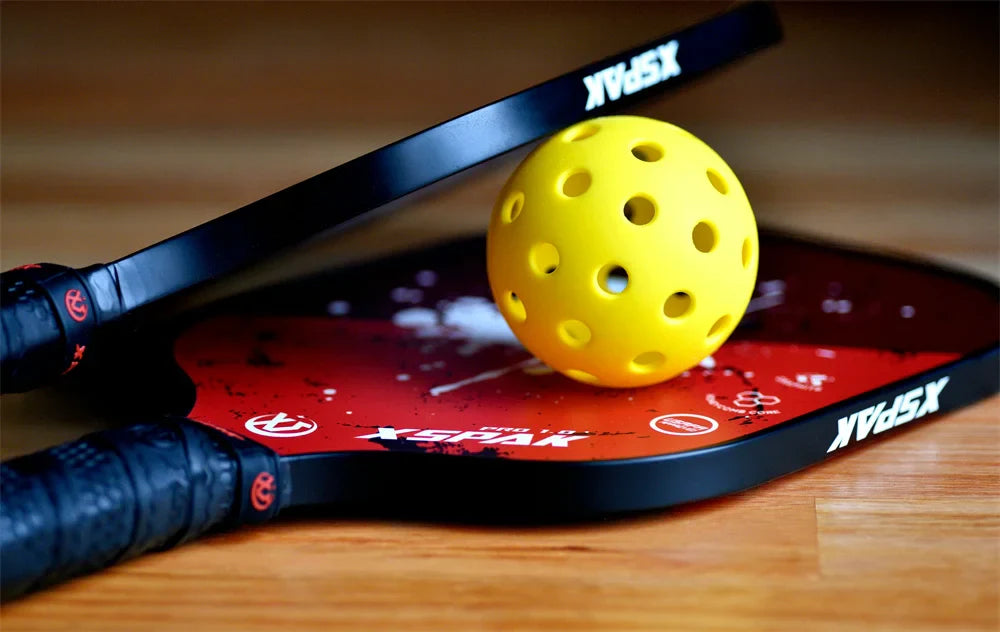 there are two cool pickleball paddles and one pickleball laying on the wooden floor